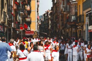A bustling street in Pamplona, Spain, during the famous San Fermin festival, capturing crowds in traditional white with red scarves.