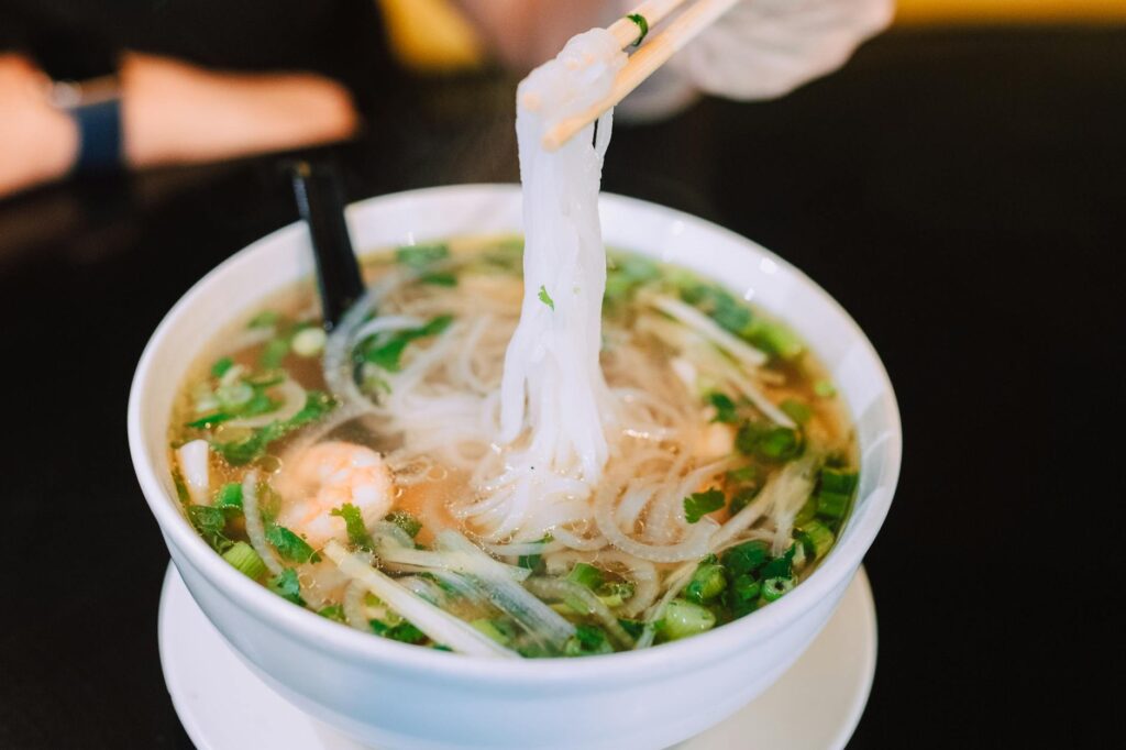 A delicious close-up of a steaming bowl of Vietnamese pho with fresh herbs and noodles.